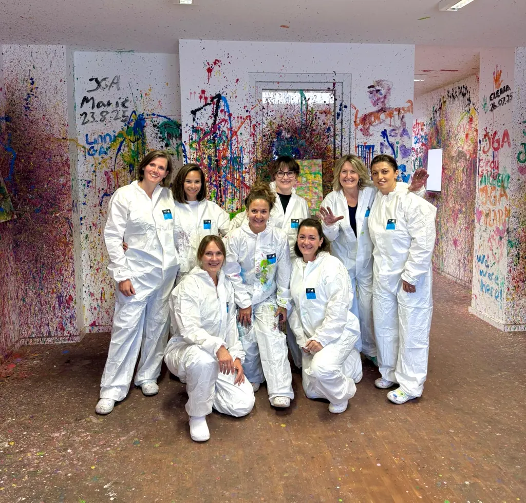 Acht Frauen in weißen Overalls vor einer Wand voller gemalter Namen