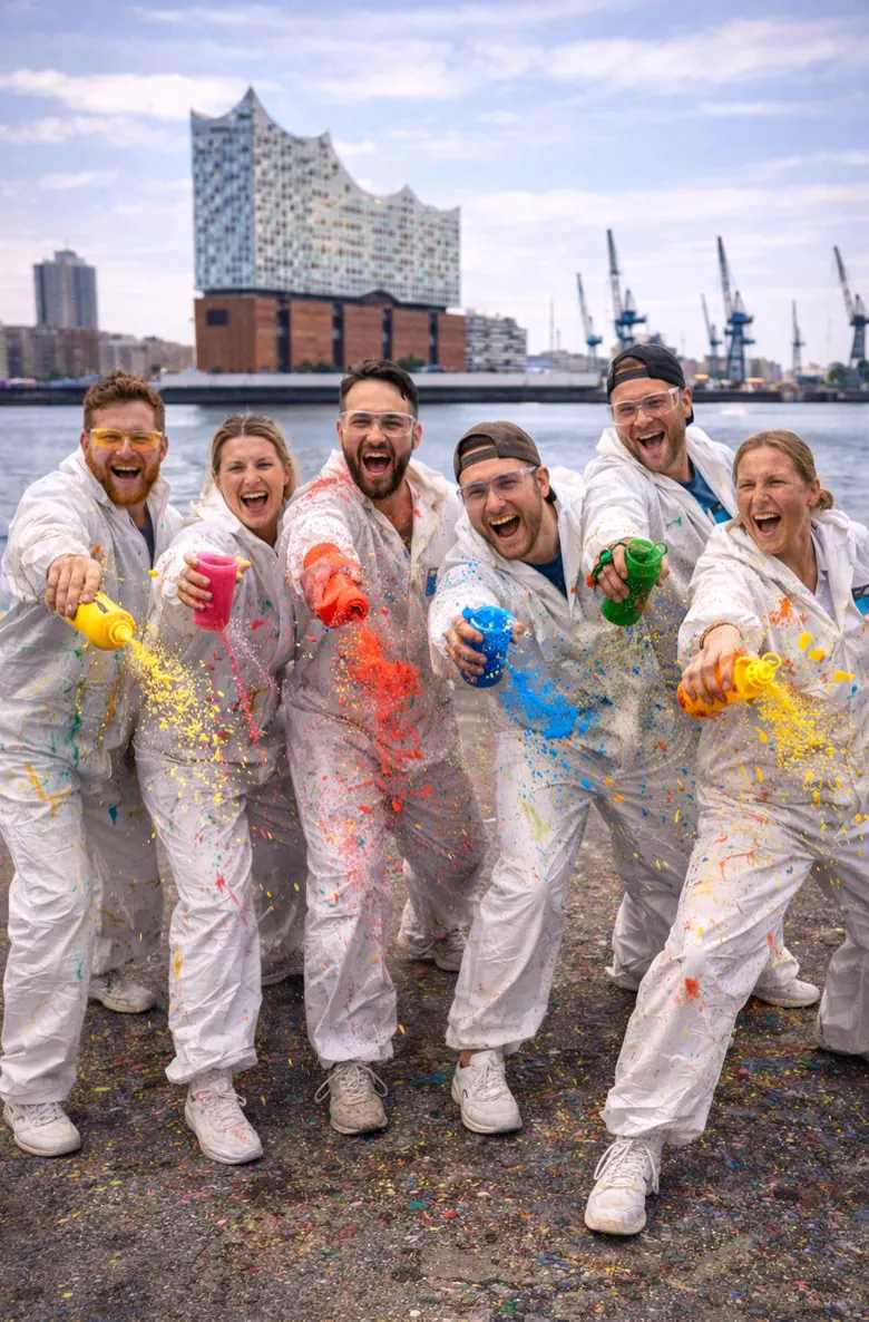 Gruppe in weißen Overalls mit fliegender Farbe vor der Elbphilharmonie